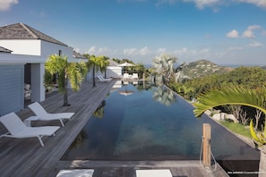 Grande piscine à débordement chauffée de 20 m, entourée d'une terrasse avec nombreuses chaises longues.
