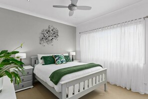 The beautifully furnished master bedroom features a queen-size bed with bedside tables and reading lamps, as well as a ceiling fan.

