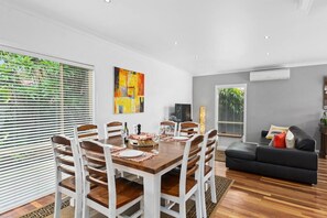 The light-filled dining area features an eight-seater table to enjoy meals together, with large windows offering leafy views out to the garden. 