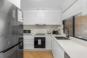 The contemporary kitchen is fully equipped and ready for your culinary creations, featuring an oven, dishwasher, microwave, fridge, coffee machine and a large window for natural light.