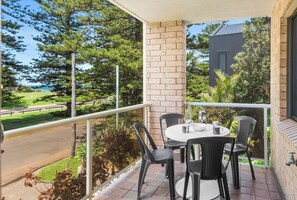 Enjoy your morning coffee or a relaxed evening drink on the second balcony, surrounded by leafy palms and towering pines, with glimpses of the ocean just beyond the treetops.