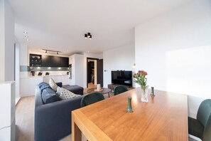 The bright living room features a pull-out sofa bed, a Smart TV, a dining table and chairs, and a small balcony