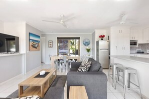 An open-plan living and dining area upstairs includes two sofas and a TV, as well as a table setting and casual seating at the breakfast bar.