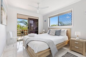 The light and airy master bedroom, located upstairs, features a queen-size bed, a ceiling fan, and direct access to the balcony.
