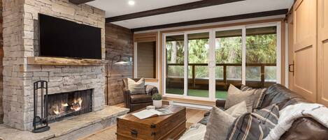 Living room with a stone-surround presto log fireplace, TV, and sliding door access to the balcony with private hot tub