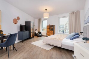A spacious living area with a bed, armchair, TV stand, and a modern décor setup.
