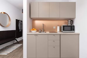 A minimalist kitchen with beige cabinets, a microwave, and warm under-cabinet lighting.
