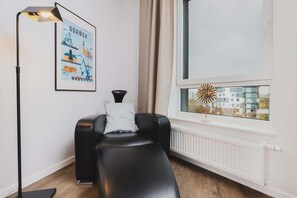 A cozy corner with a black leather armchair, a framed artwork, and a window.
