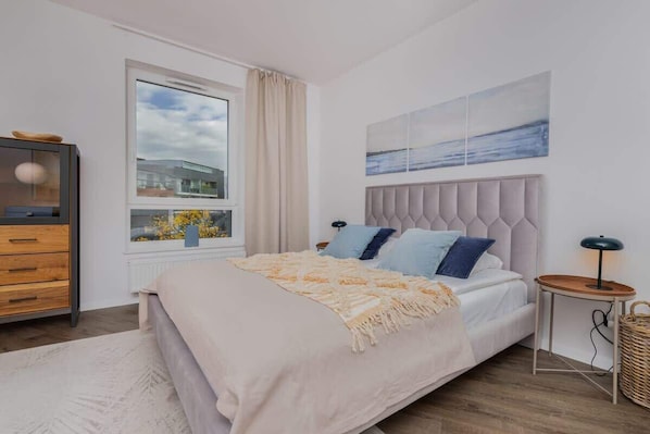 A bright bedroom with a large bed, soft bedding, and a window offering a city view.
