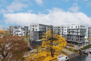 A city view from the window, showing modern apartment buildings and autumn trees.
