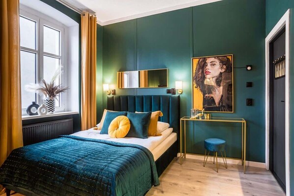 A stylish bedroom with teal walls, a gold-accented bed, and decorative pillows.

