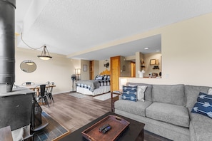 Living area with floor to ceiling windows, wood-burning fireplace, flat screen TV, hardwood flooring and cozy sectional which pulls out to offer an additional queen-sized bed.