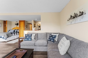 Living area with floor to ceiling windows, wood-burning fireplace, flat screen TV, hardwood flooring and cozy sectional which pulls out to offer an additional queen-sized bed.