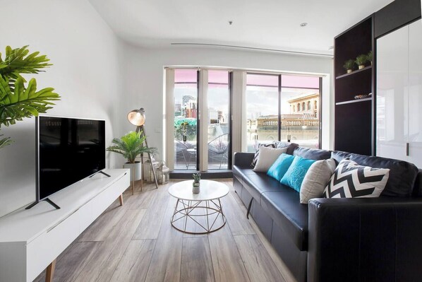 An open-plan space features a living area furnished with a sofa that doubles as a sofabed, vintage-style armchair, marble-topped coffee table and a wide-screen TV with Netflix.