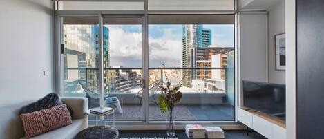 The bright and open living room with floor to ceiling glass doors incorporates soft colours and indoor plants.