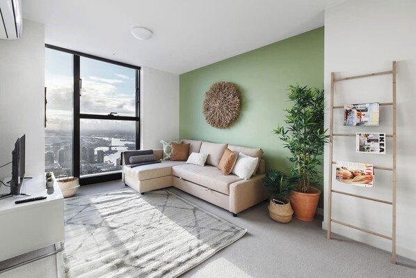 Embrace the serene charm of this sunlit living room, featuring a fold-out sofa bed and sweeping city views.