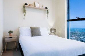 Cozy, minimalist bedroom featuring a comfortable queen bed, soft natural light, and stunning coastal and city views.