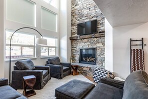 Experience the cozy living room, outfitted with plush seating, an expansive smart TV, and two-story windows that frame the breathtaking mountain vistas.