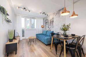 A stylish open-plan living area with a blue sofa, dining table, and warm lighting.

