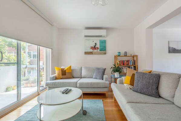 A bright living room features sleek furniture, two plush couches and a 42” HDTV with a Samsung surround system.