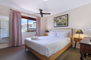 The master bedroom comes furnished with a plush queen bed, a ceiling fan and a large window with a view.
