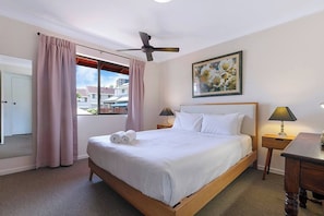 The master bedroom comes furnished with a plush queen bed, a ceiling fan and a large window with a view.
