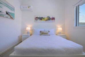 The spacious primary bedroom boasts a cosy queen bed and ample storage, enveloped in natural light.
