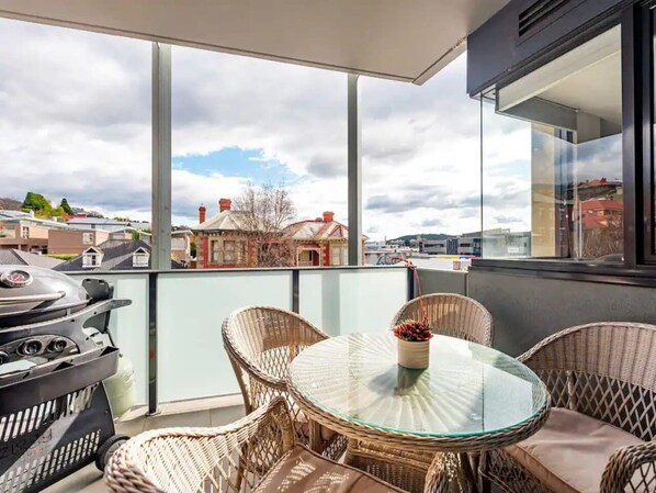 Step onto the large covered balcony, furnished with a four-seat outdoor table setting and a BBQ grill. 