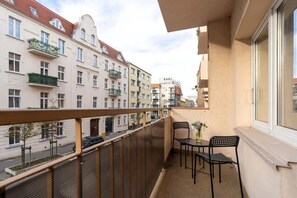 A balcony with outdoor seating, overlooking a European-style residential street.

