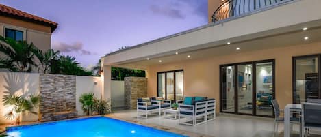 Private backyard by night with pool, dining table and conversation set