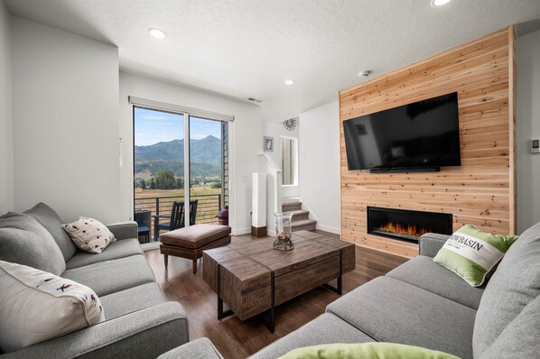 Experience the cozy living room, outfitted with plush seating, an expansive smart TV, and sliding patio doors that frame the breathtaking mountain vistas.