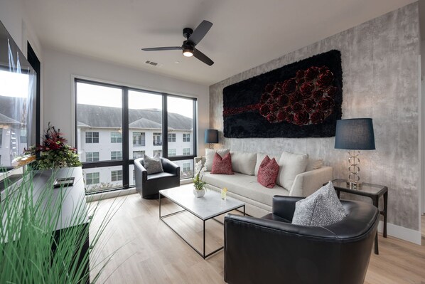 Modern open concept living area with floor to ceiling windows, designer furniture, smart TV, and access to private patio.