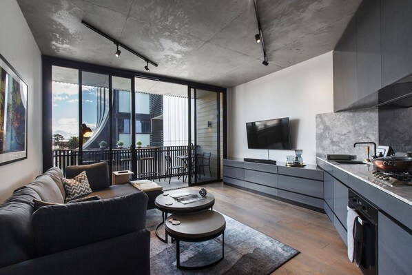 A living area has an expansive sectional sofa, monochromatic coffee table a wall-mounted, flat-screen TV