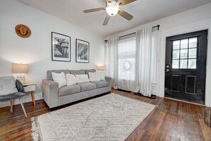 Cozy living room with a gray sofa, a soft textured rug, and wooden flooring, a ceiling fan and light fixture adding warmth.