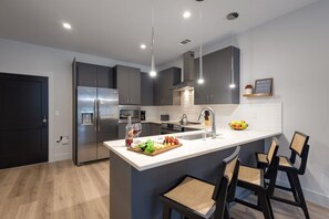 Fully equipped kitchen with stainless steel appliances, basic cooking essentials, toaster, coffee machine, and kitchen bar seating.