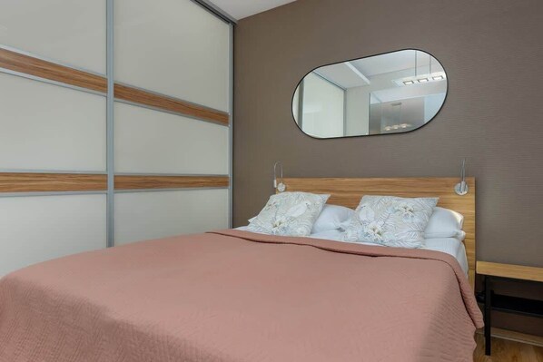 A cozy bedroom with a pink bedspread, a wooden bed frame, and a sliding-door wardrobe.