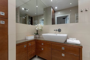 A bathroom with beige tiles, a large mirror, and a wooden vanity unit.