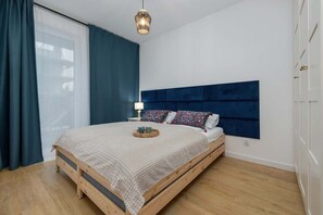 A bedroom with a beige bedspread, blue headboard, and dark curtains.
