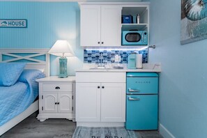Cute kitchenette filled with glasses, silverware, coffee maker, plates, cups, microwave, mini fridge and freezer, paper towels, soap, blender, toaster and more!