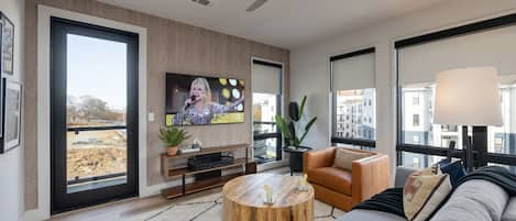 Bright open living space featuring a smart flat-screen TV, designer furnishings, and access to a private balcony.