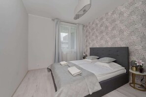 A bedroom with a grey upholstered bed, patterned wallpaper, and elegant bedding.
