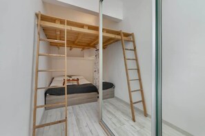 Bedroom with a loft-style setup, featuring a wooden ladder leading up to a bed. The space has white walls and a minimal design, with an emphasis on functionality.