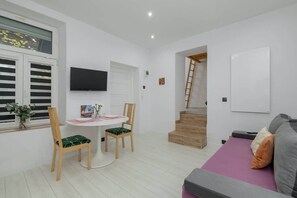 Living room area with a sofa, white walls, and wooden elements. There are stairs leading up to an additional space, and the overall ambiance is modern and clean.