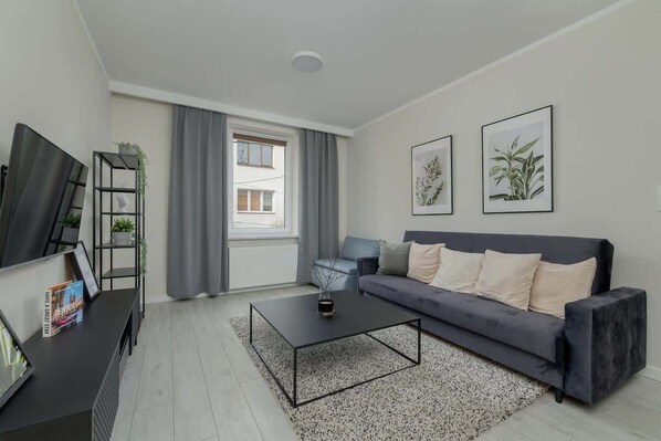 A modern living room with a comfortable grey sofa, a flat-screen TV, and minimalist wall art, creating a cozy yet stylish atmosphere.

