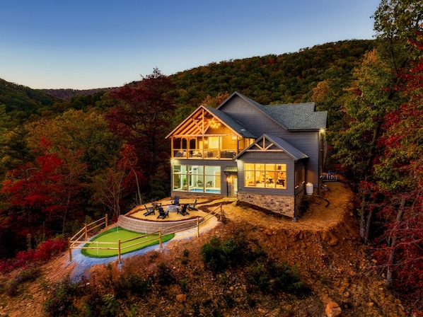 A stunning 5 bedroom luxury Smoky Mountain retreat featuring panoramic views, private putting green, gas firepit, indoor pool, hot tub, outdoor giant chess set, game room, and theater room.