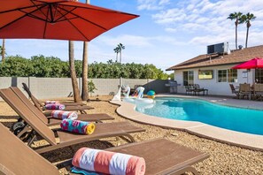 Spacious backyard featuring a heated pool with playful toys and a basketball hoop, set up for both relaxation and fun.

