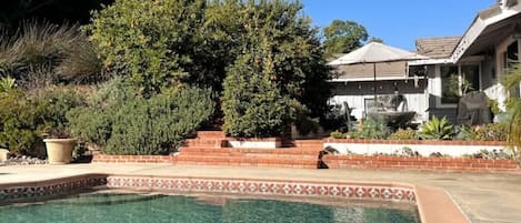 Back yard with pool/hot tub, sitting area, dining area and lush landscape. 