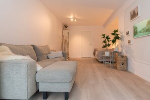 Spacious and light-filled studio with a modern grey sofa and warm wooden floors — ideal for couples or solo travelers.