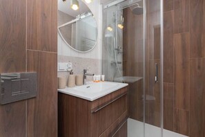 A modern bathroom with rich wooden paneling, a spacious glass shower enclosure, and a sleek vanity unit under a round mirror.

