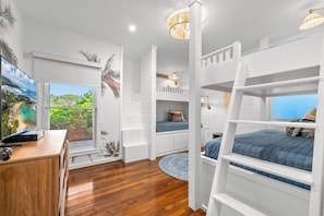 Bright bunk bedroom with ocean views, tropical decor, and cozy blue bedding.